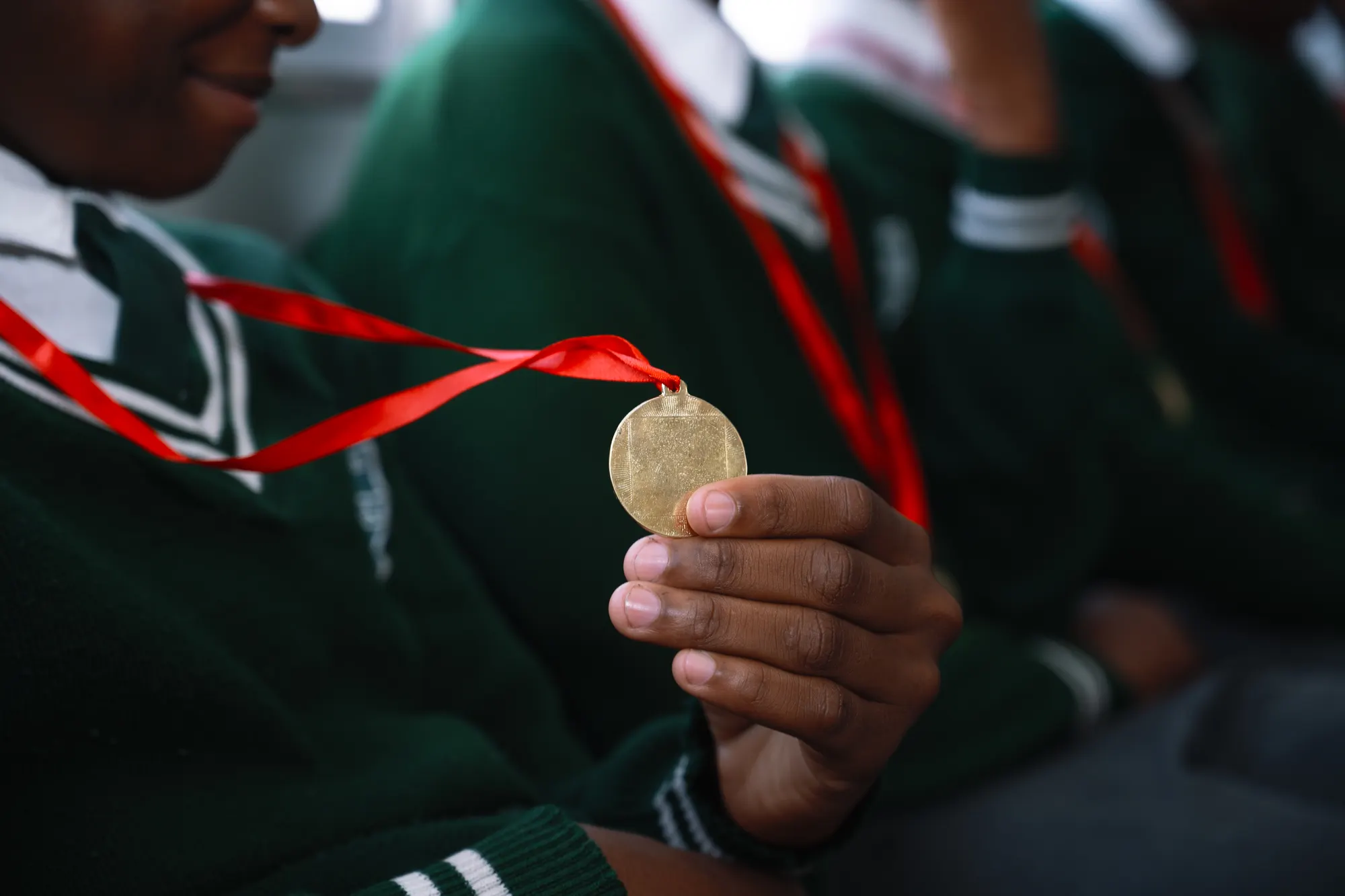 A learner holding a gold medal on a red ribbon