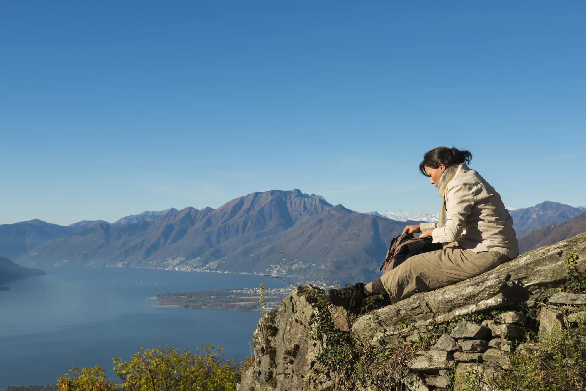 A hiker resting on a rocky outcrop above a lake and mountain range